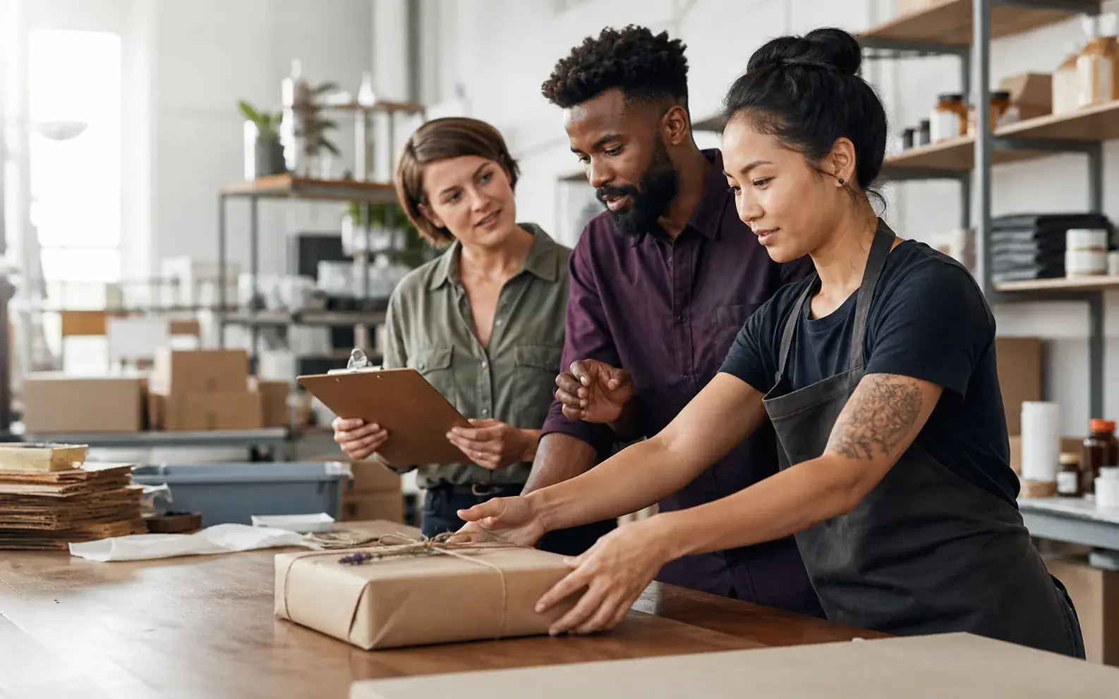 A small team moves a finished package along a workbench while discussing the next step in their process.